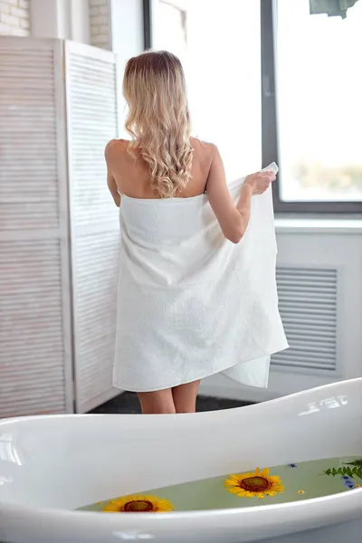 Молодая стройная блондинка сушит тело полотенцем после душа, вид сзади — стоковое фото