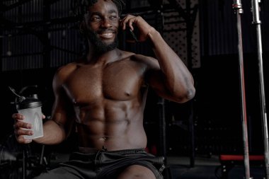 Rahatlamış Afro-Amerikalı adam telefonda konuşuyor, spor salonunda dinlenme eğitimi alıyor.
