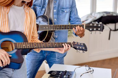 Çift gitar çalmayı öğreniyor. Erkek öğretmen bayan öğrenciye açıklar.