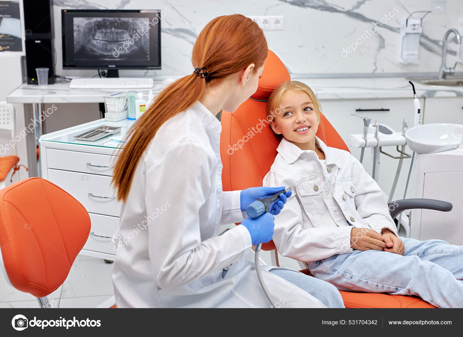 Dentist in gloves holding dental drill while treating child girl