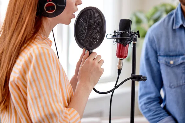 Рыжеволосая женщина, поющая под микрофон в студии. Женский вокал. Вид сбоку — стоковое фото