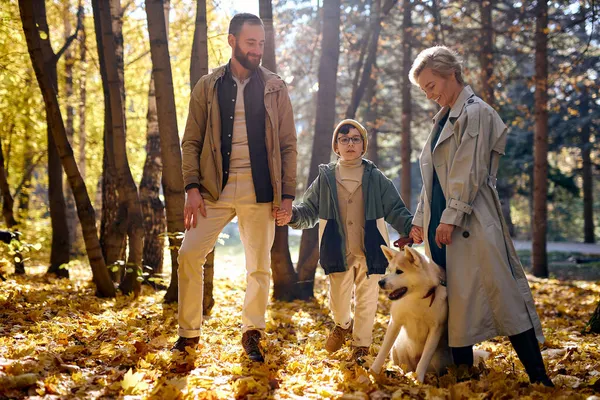 Fröhliche Familienwanderung mit Sohn und weißem Haustier im herbstlichen Wald. Familie, Freundschaft — Stockfoto