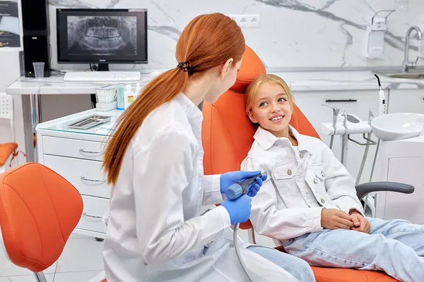 Tandläkare i handskar som håller tandborr vid behandling av barn flicka patient på tandläkarmottagningen — Stockfoto