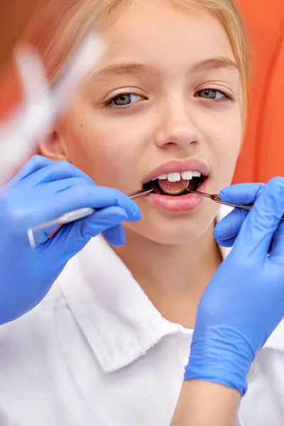 Чарівна дівчинка сидить у медичному кріслі, а стоматолог фіксує зуби за допомогою інструментів — стокове фото