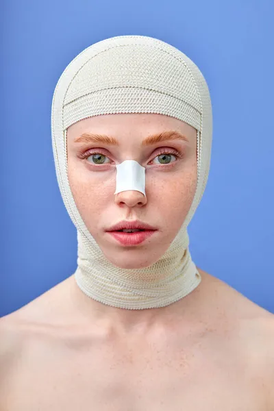 Kvinnligt ansikte i medicinska bandage efter operation på blå studio bakgrund. kopieringsutrymme — Stockfoto