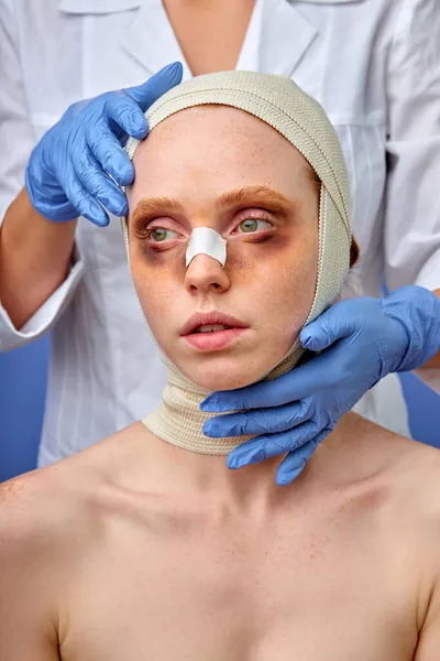 Kvinna med bandage över huvudet, läkare vidrör efter operation. isolerad blå bakgrund, studio skott — Stockfoto