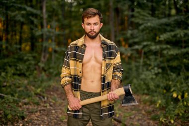 Açık ekose gömlekli yakışıklı beyaz adam büyük bir balta taşıyor.