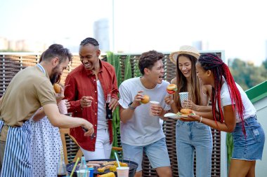 Uluslararası öğrenciler barbekü verandasında hamburger yiyip limonata içiyorlar.