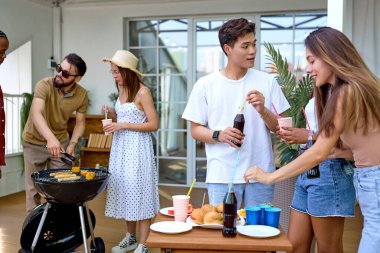 Sıradan yaz kıyafetleri içinde heyecanlı genç kadınlar ve erkekler parti sırasında eğleniyor.