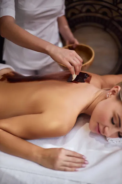 Massagist covers the female back with melted chocolate. Spa procedure chocolate wrap. — Stock Photo, Image