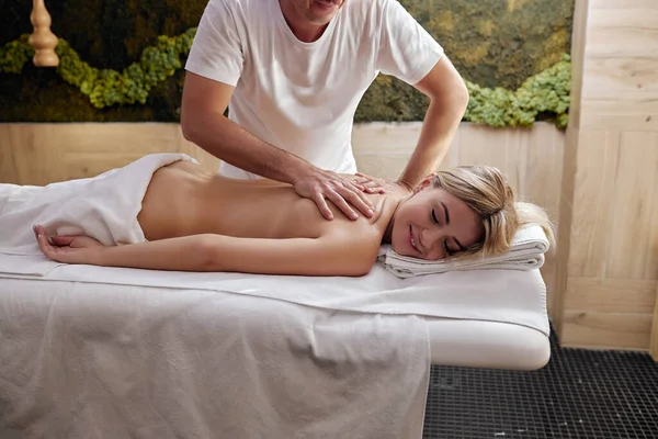 Manos para hombre hacen masaje de espalda de columna terapéutica para mujer acostada en un sofá de masaje —  Fotos de Stock