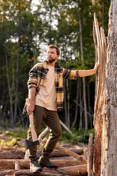 Modern logger. ranch man carry axe, stand by tree. sexy guy in plaid shirt in forest