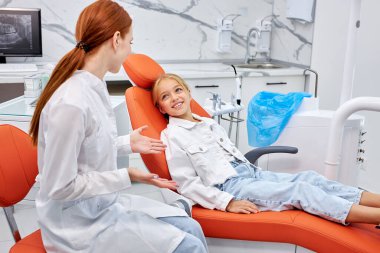 Profesyonel dişçi dişlerini kontrol ederken güzel çocuk hastalarıyla iletişim kuruyor.