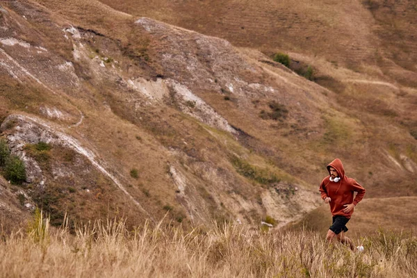 Motivierter Mann im Kapuzenpulli läuft auf dem Feld, joggt, treibt Sport, Fitness — Stockfoto