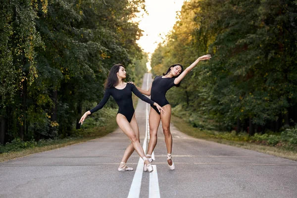 Dvě štíhlé ženy s dokonalým tělem v černé tutu tanec na cestě lesa — Stock fotografie