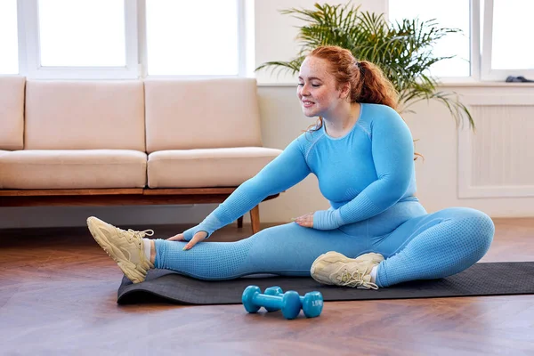 超重女性伸展腿，在瑜伽垫上运动，过着积极的生活 — 图库照片