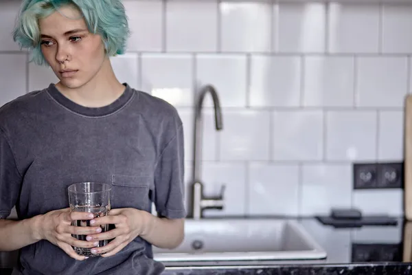 Schöne kaukasische Frau trinkt Wasser in Küche, allein zu Hause, melancholisch — Stockfoto