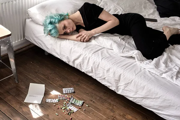 Selbstmord durch Medikamentenüberdosis. Pillen auf dem Boden und junge Frau mit Depressionen — Stockfoto
