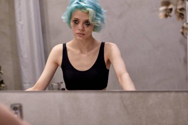 Depresyondaki genç kadın aynadaki yansımaya bakarak banyoda ağlıyor.