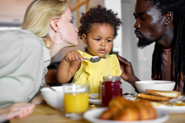 Χαριτωμένο μαύρο κοριτσάκι απολαμβάνοντας πρωινό με τους γονείς στο σπίτι, τρώγοντας χυλό — Φωτογραφία Αρχείου
