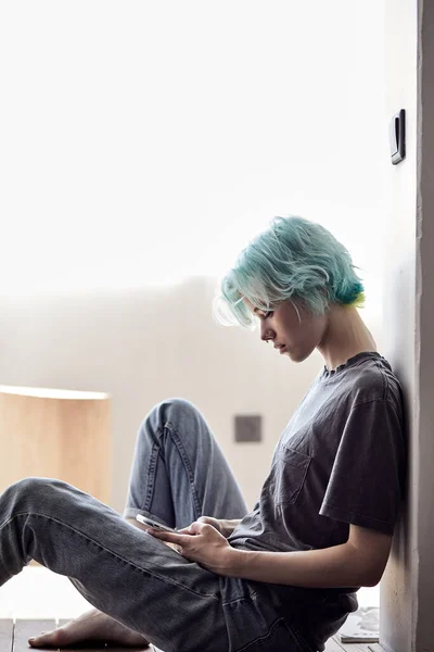 Attraktive junge Frau mit deprimiertem Gesichtsausdruck, die auf dem Boden sitzt und ihr Telefon hält — Stockfoto