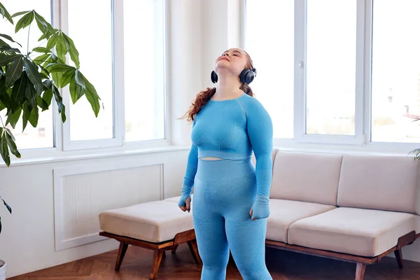 Fet kvinna Lyssna på musik och göra övningar för stretching hals, Sport inomhus hemma — Stockfoto