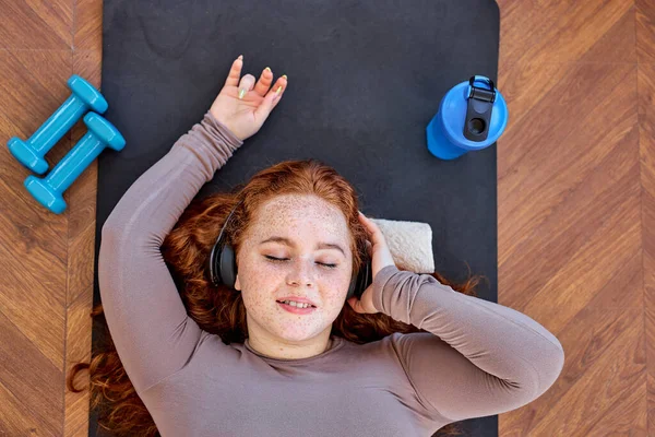 Kızıl Saçlı Kadın 'ın üstünde spor üstüne müzik dinlerken, yoga egzersizleri yaparken, dinlenirken — Stok fotoğraf