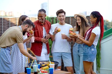 Mutlu arkadaşlar hamburger yer ve barbekü verandasında limonata içer.