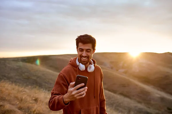 Ajuste o smartphone masculino feliz do uso ao caminhar no campo que faz uma ruptura — Fotografia de Stock