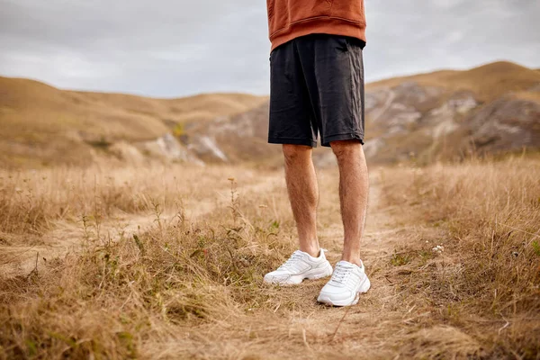 Masculino recortado en pantalones cortos y zapatillas de deporte de pie en la hierba, tranquilo, sin movimiento —  Fotos de Stock