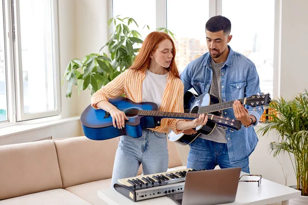 Красивый мужчина учит девушку играть на гитаре. Парень показывает женщине, как играть на гитаре. — стоковое фото