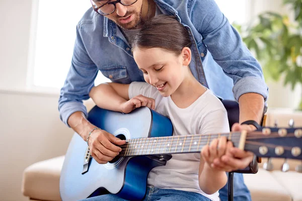Şirin küçük kız ve yakışıklı baba evdeki kanepede oturmuş gitar çalıyorlar. Babalar Günü.