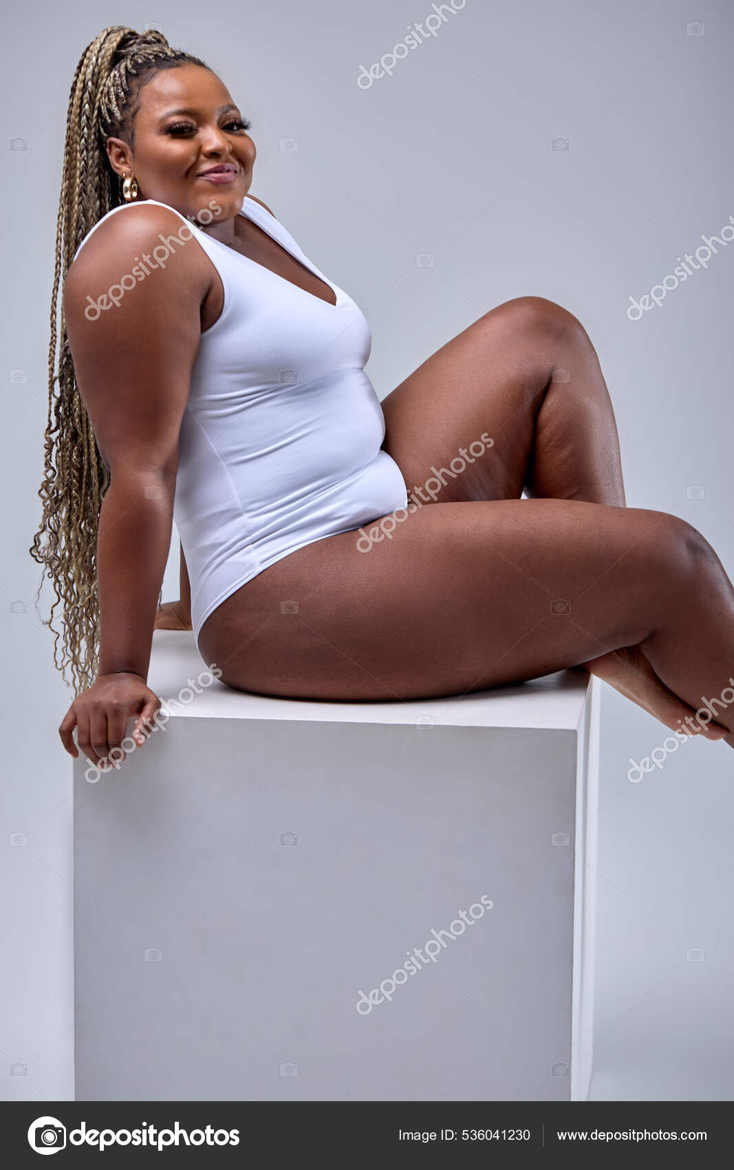 Cheerful plus size black woman in bodysuit laughing, lsitting in