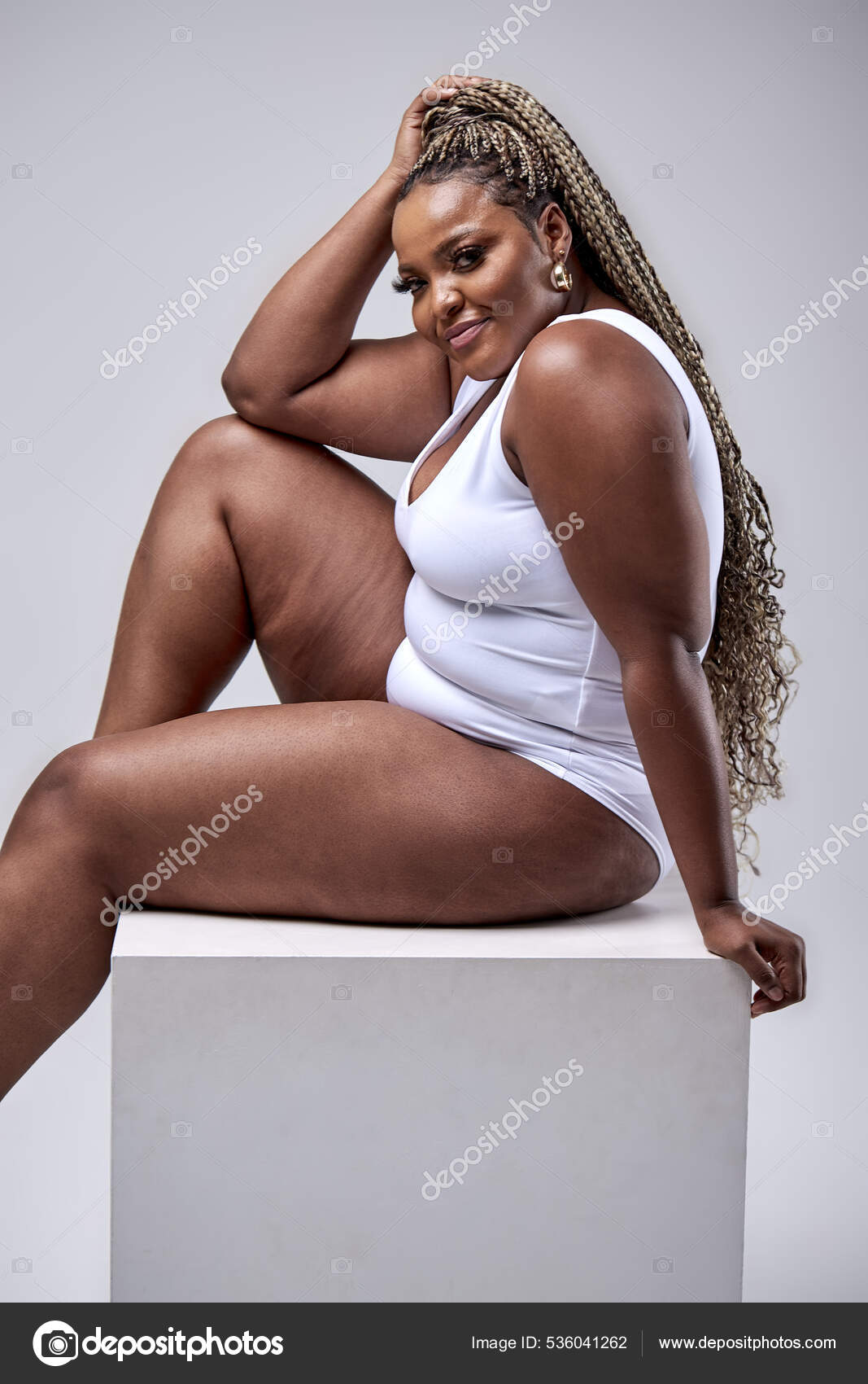 Plus size modelo sexy e feliz em bodysuit branco posando no cubo