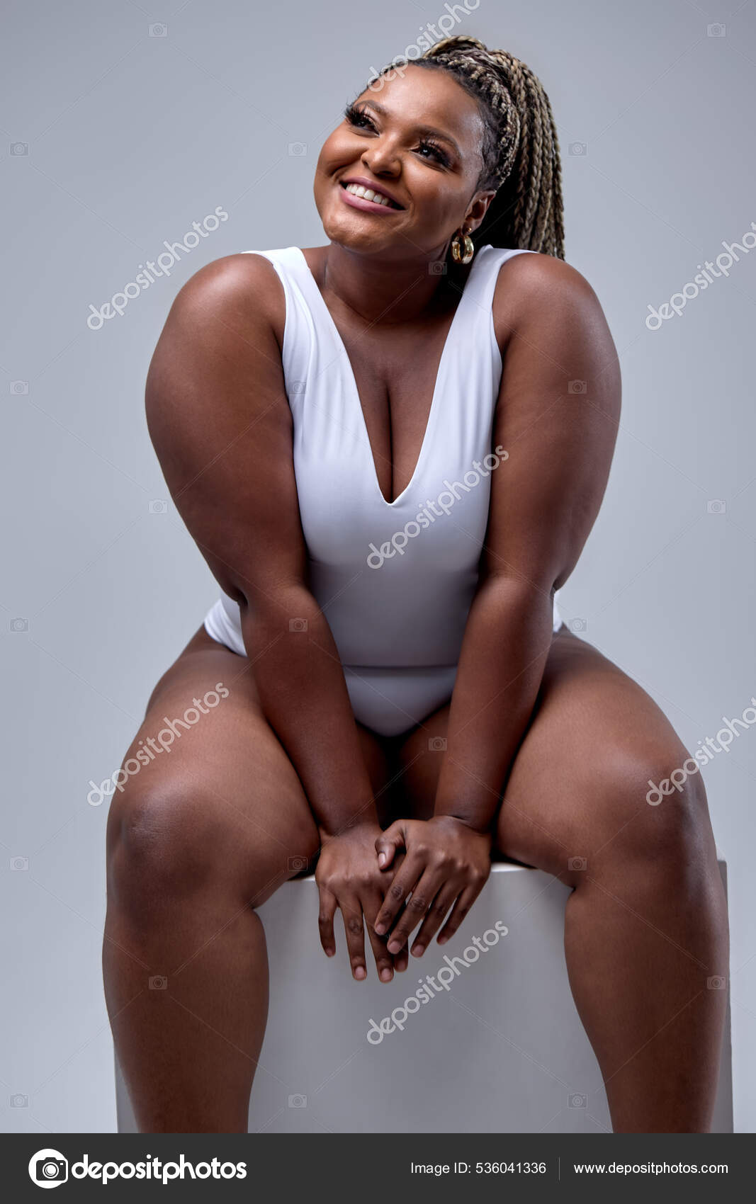 Cheerful plus size black woman in bodysuit laughing, lsitting in studio  over white Stock Photo by ©romanchazov27 536041336