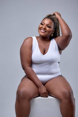 Beyaz elbiseli şişman bir kadın beyaz arka planda kameraya poz veriyor.