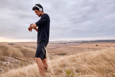 Siyah eşofmanlı genç adam dışarıda egzersiz yapmadan önce zamanı kontrol ediyor.