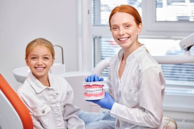 Diş hekiminin portresi. Diş sağlığı kliniğinde çene yapısı ve tatlı kız çocuğu.