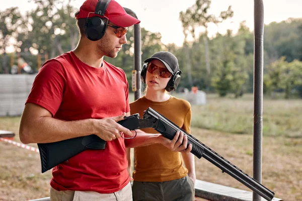Caucásico hombre enseñar mujer a recargar un rifle en tiro campo al aire libre — Foto de Stock