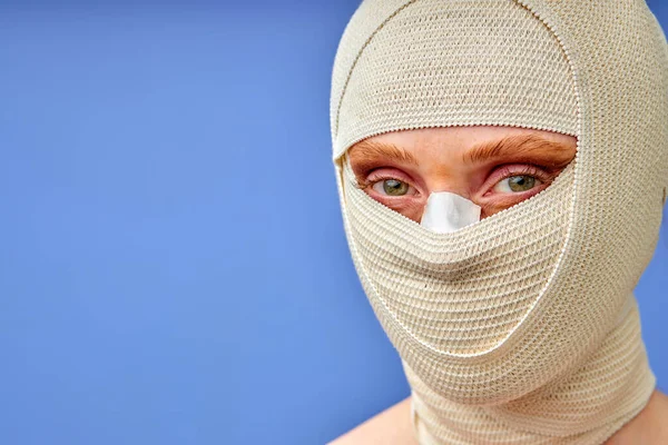 Mulher bonita após cirurgia plástica com rosto enfaixado, isolado em fundo azul — Fotografia de Stock