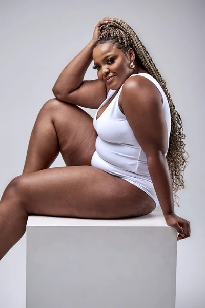 Cheerful plus size black woman in bodysuit laughing, lsitting in studio  over white Stock Photo by ©romanchazov27 536041336