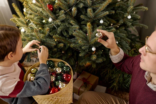 Küçük oğlunun Noel ağacını oyuncaklarla süslemesine yardım eden mutlu genç adam.