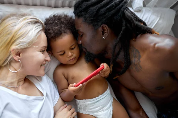 Adorable negro hija niño tener divertido con padres viendo vídeo en smartphone — Foto de Stock