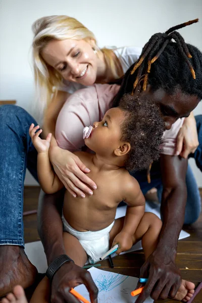 Liebevolle junge Eltern, die auf dem Boden sitzen, haben Spaß beim Malen mit ihrer kleinen Tochter. — Stockfoto