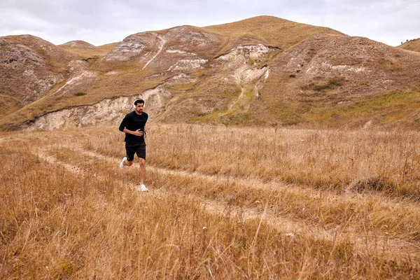 Fokussierter Mann im schwarzen Trainingsanzug läuft morgens auf dem Feld, treibt Sport — Stockfoto