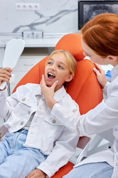 Redhead γυναίκα οδοντίατρος με στολή εργάζεται με παιδί ασθενή στο οδοντιατρείο — Φωτογραφία Αρχείου