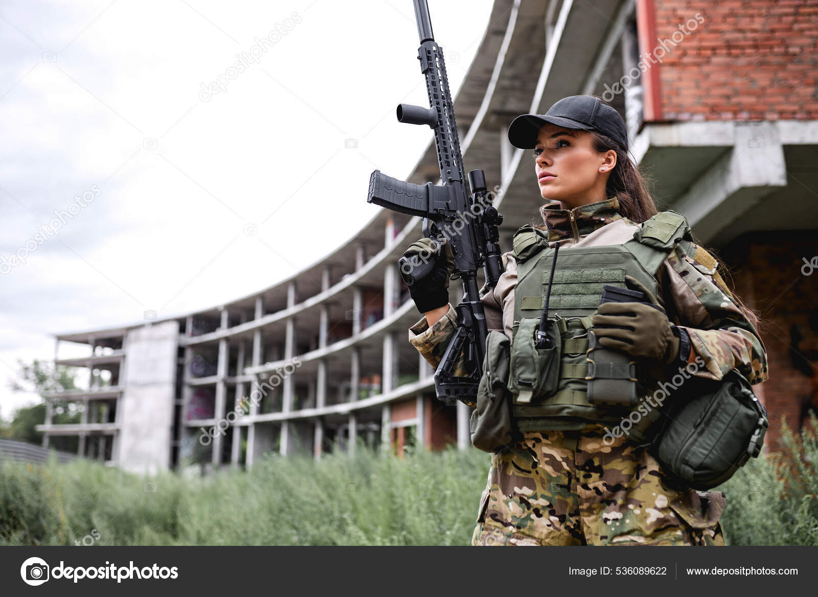 Military lady woman in tactical gear posing for photo in grass next to  abandoned building Stock Photo by ©romanchazov27 536089622