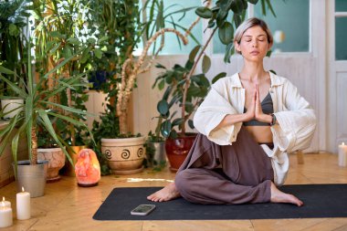 Genç sağlıklı kadın evde lotus poz vererek yoga yapıyor.