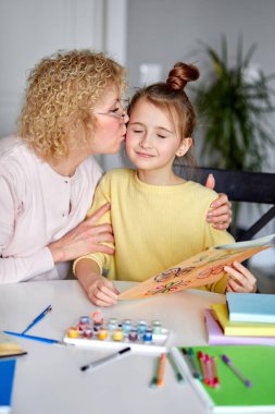 Güzel güzel kız ve büyükanne evdeki masanın arkasında oturuyor, bir kadın yanaktan öpüşüyor.
