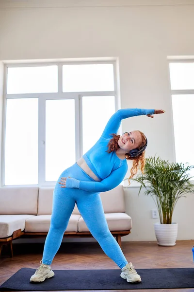 Aşırı kilolu kadın evde yoga ya da spor egzersizlerinden önce kaslarını ısıtıyor. — Stok fotoğraf